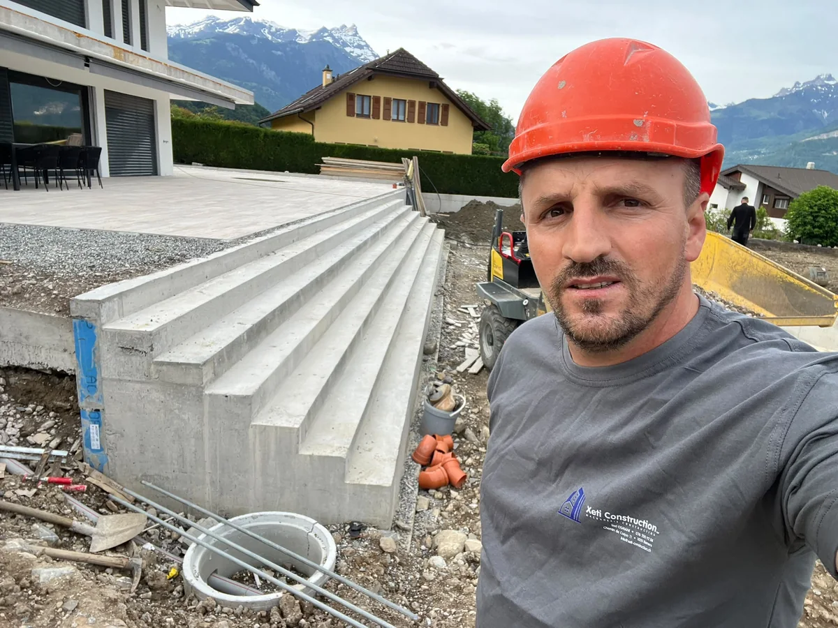 Un professionnel XETI portant un casque rouge devant un escalier extérieur en béton