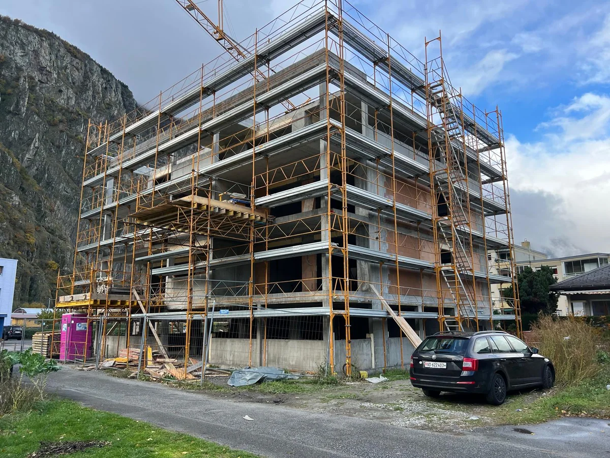 Immeuble en construction entouré d’échafaudages devant les montagnes